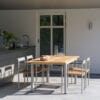 Brafab Lyon-puutarhapöytä 152 cm, tiikkikansi ja vaaleanharmaan väriset metallijalat. Miljöökuvassa terassilla DK-tuolien kanssa.