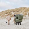 SACKit Soft Sofa -nojatuolit, miljöökuvassa mies ja nainen kävelevät hiekkarannalla ja vetävät sohvamoduuleja kärryssä perässään. Vihreä (olive) kangas.