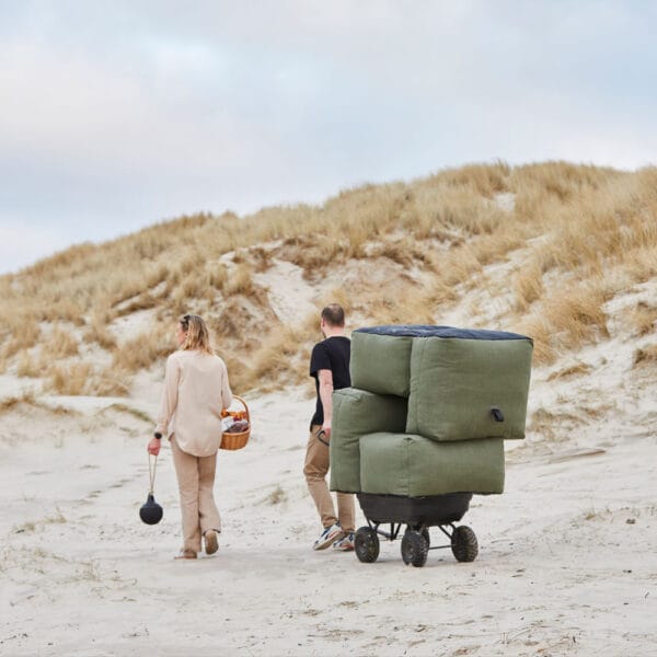 SACKit Soft Sofa -nojatuolit, miljöökuvassa mies ja nainen kävelevät hiekkarannalla ja vetävät sohvamoduuleja kärryssä perässään. Vihreä (olive) kangas.