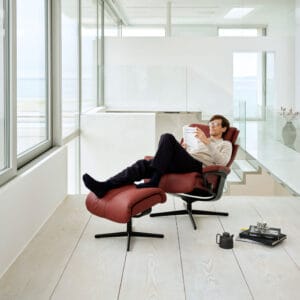 Stressless Magic-lepotuoli tummanpunaisella nahkaverhoilulla ja mustalla Cross-jalalla, Miljöökuvassa mies lepää tuolilla lukien kirjaa.