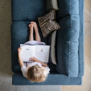 Rowico Langdon-sohva, sininen. Miljöökuva ylhäältäpäin, lapsi istuu sohvalla lukemassa kirjaa.
