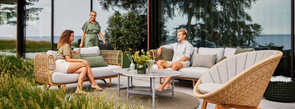 Artikkelikuva | Cane-line Nest-sarjan ulkosohva ja nojatuoli, Peacock-nojatuoli. Miljöökuva ihmisillä.